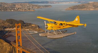 yellow seaplane flying above the golden gate bridge with the water