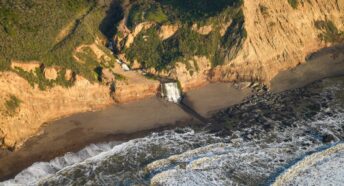 northern california coastline from the air where you can see a river turn into a waterfall flow into the pacific ocean