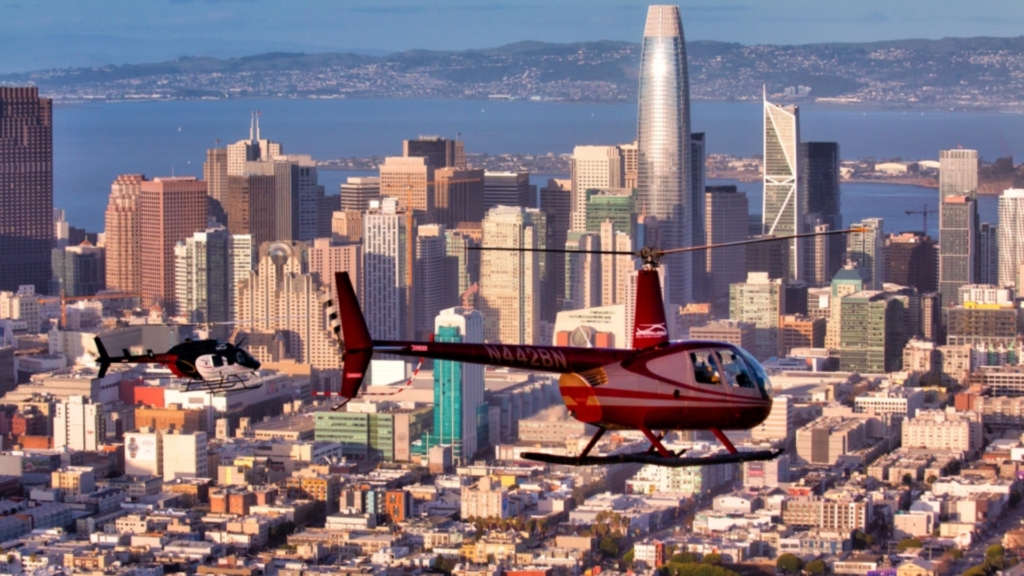 two red helicopters flying above san francisco with the skyline and bay in the background