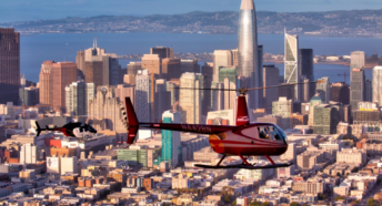 two red helicopters flying above san francisco with the skyline and bay in the background