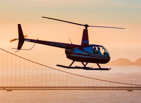 helicopter soaring above golden gate bridge at sunset