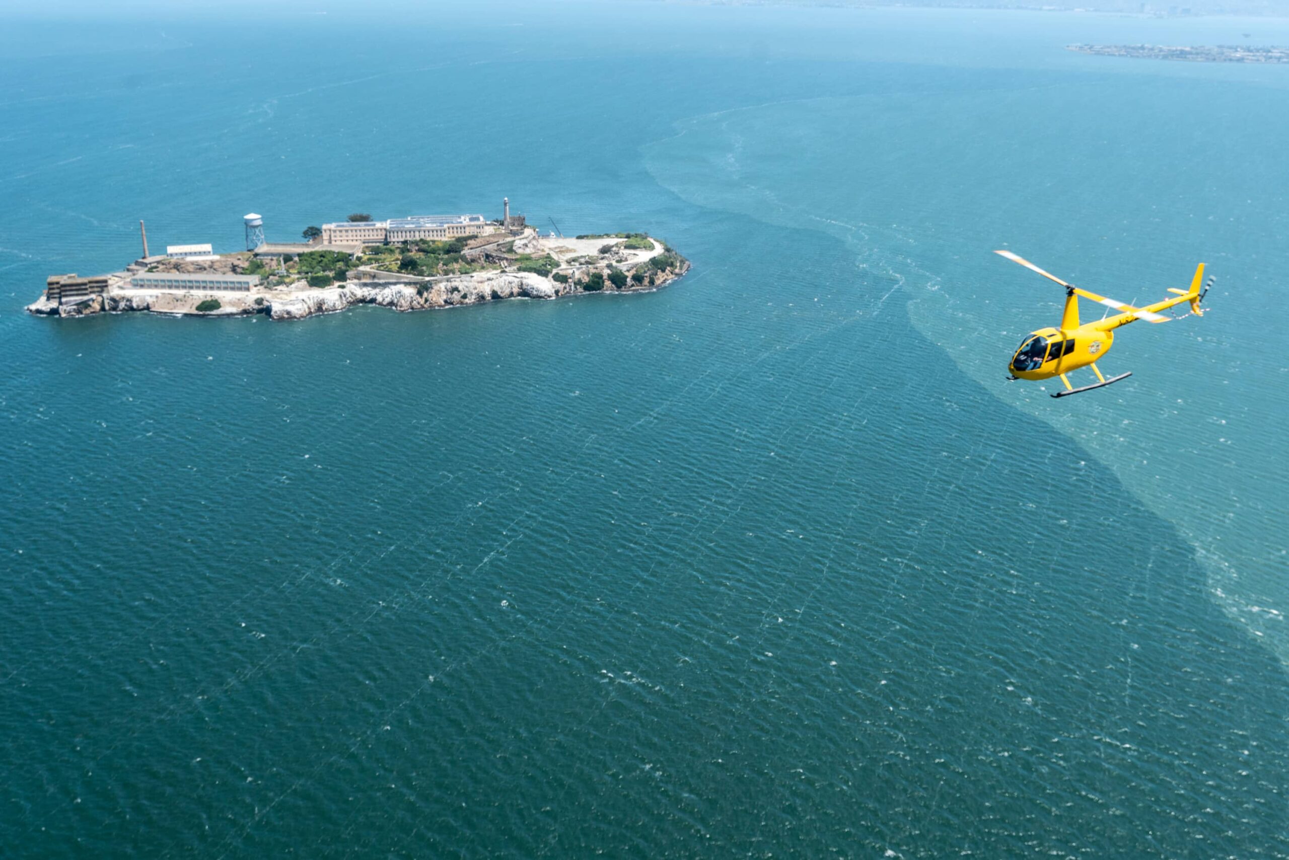 A yellow helicopter flies over Alcatraz in San Francisco
