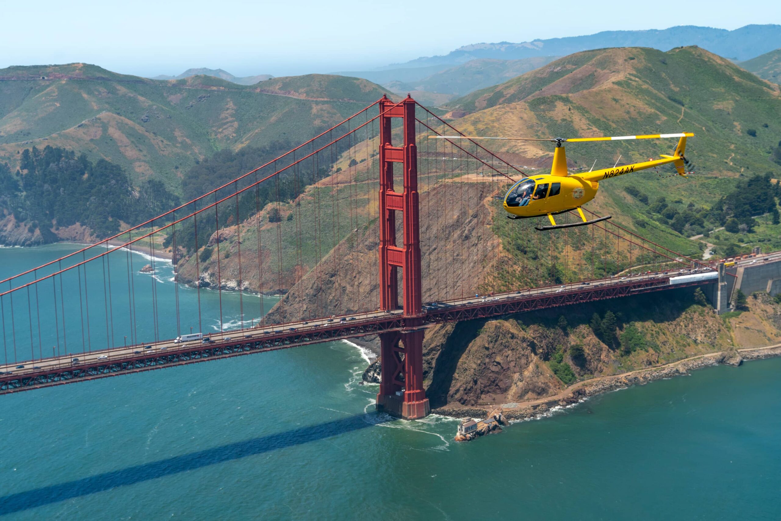 A yellow helicopter flies near the Golden Gate Bridge in SF