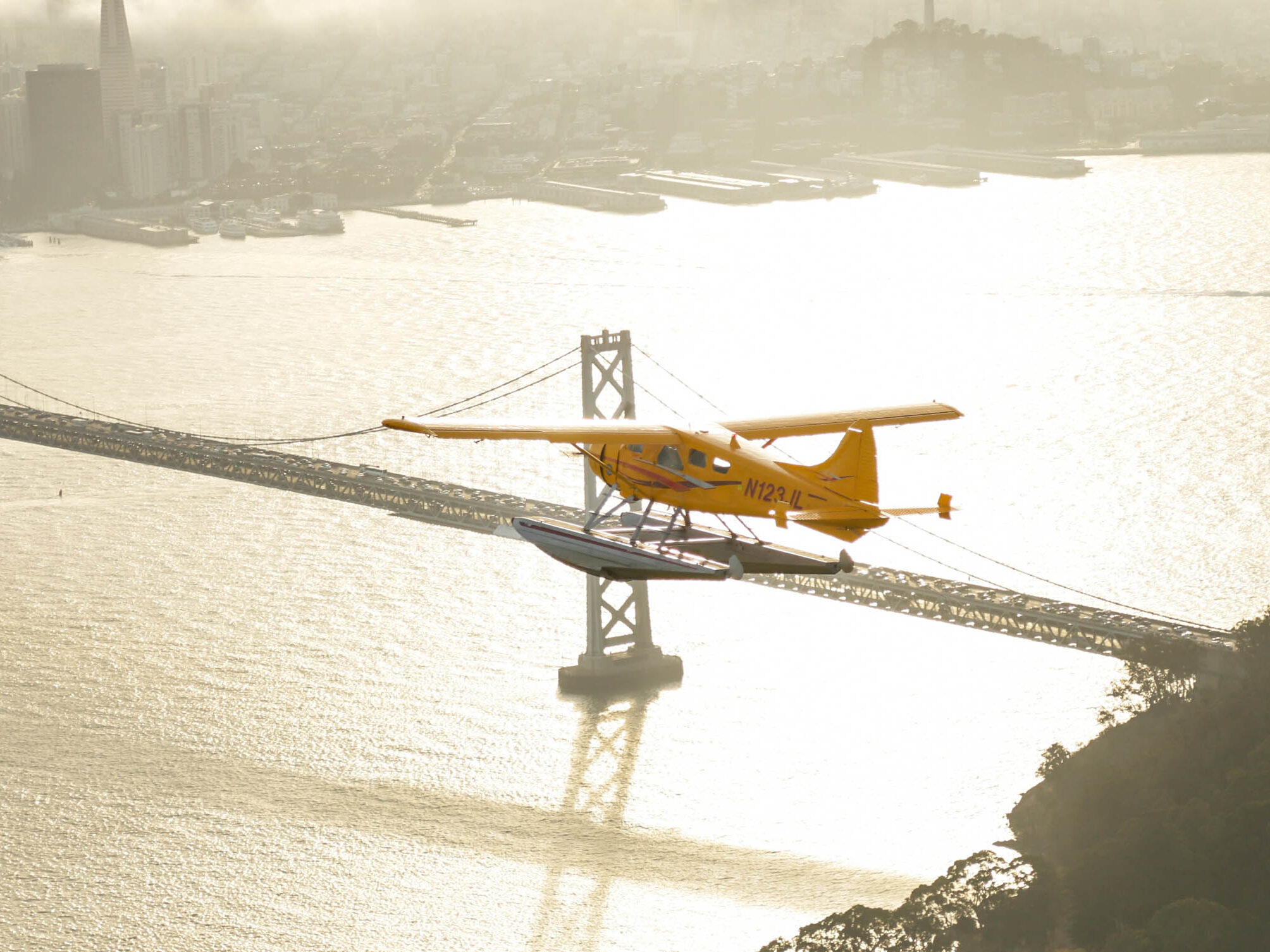 A yellow seaplane flies over the water of San Francisco