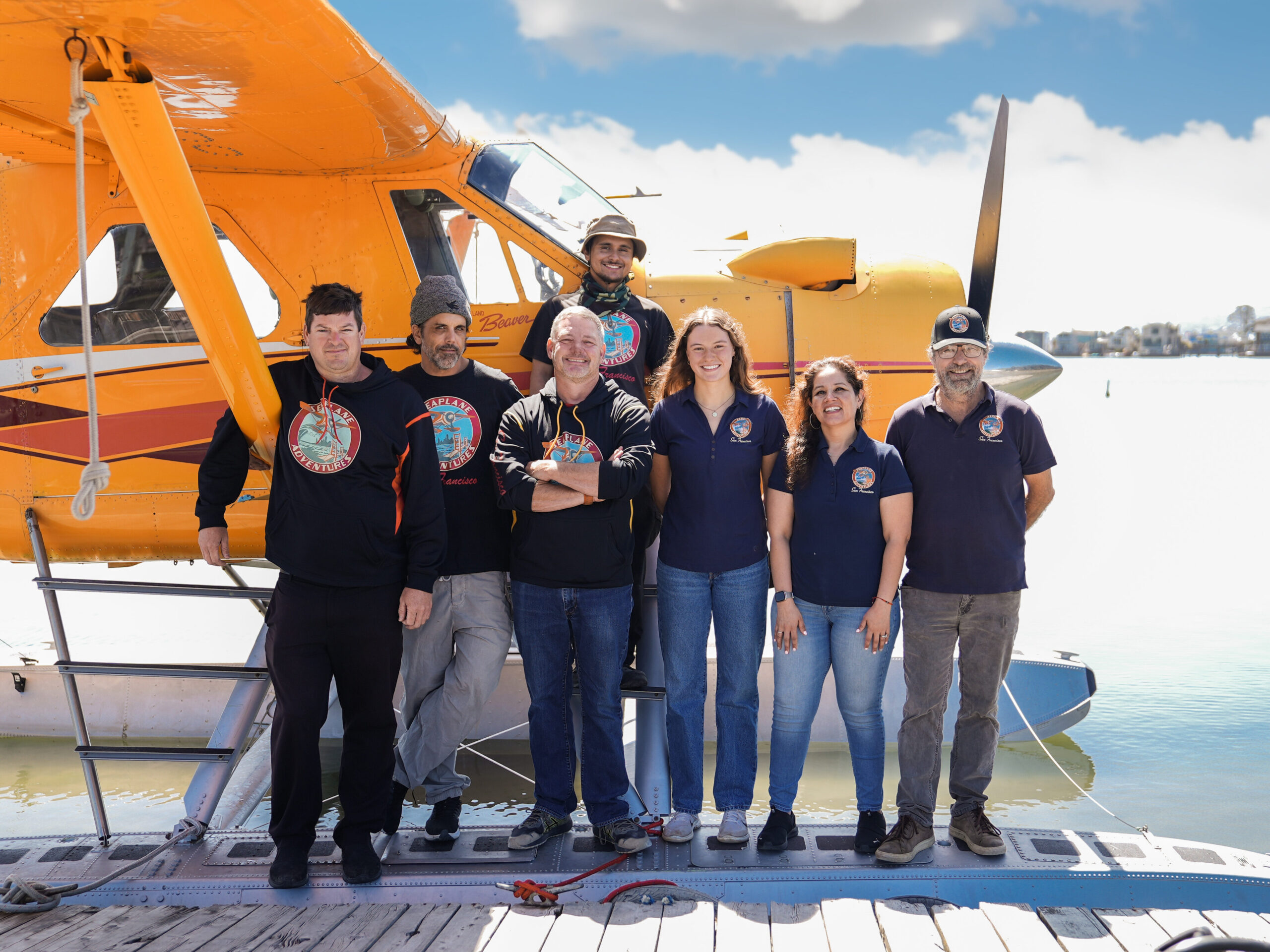 Employees of Seaplane Adventures smile in front of a yellow seaplane